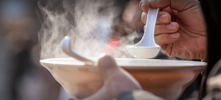 Mann hält Suppenteller mit einer Steinsuppe in der Hand und einen Löffel